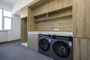 A laundry room with two washing machines, wooden cabinetry, and a countertop. - Taiyue Pearl Business Hotel (Qinyuan)