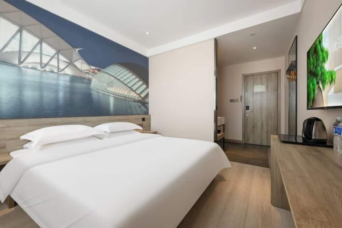 Ein modernes Hotelzimmer mit einem großen Bett, einem Holztisch und Wandgemälde eines Gebäudes.