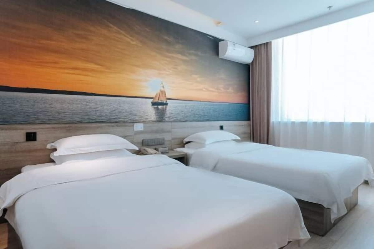 Ein Hotelzimmer mit zwei Betten, einer Sonnenuntergangsmalerei an der Wand und einem großen Fenster mit Vorhängen.