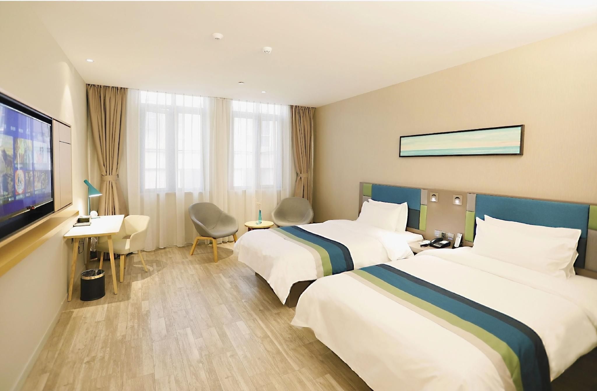 Ein Hotelzimmer mit zwei Betten, einem Schreibtisch, einem Stuhl, einem Fernseher und einem Bild an der Wand.