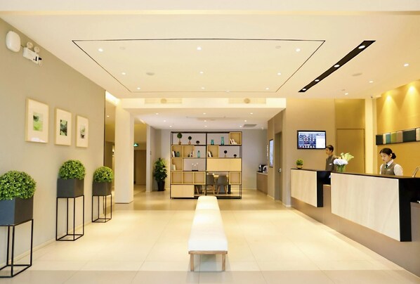 Zona de recepción de un hotel con mostrador, una banca de espera y una estantería con diversos objetos.