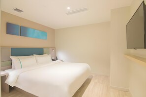 A hotel room with a large bed, a flat-screen TV mounted on the wall, and a modern headboard.
