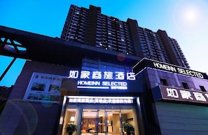 Un hotel con un llamativo letrero que dice 'HOMEINN SELECTED', un amplio acceso de vidrio y una fachada de edificio moderna.