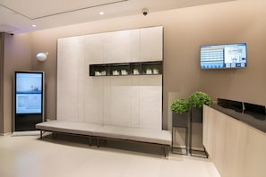 A modern reception area with a bench, a digital display, and a wall-mounted shelf with potted plants.