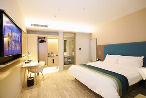 Una habitación de hotel con cama, escritorio con silla, televisión y baño.
