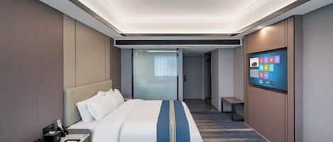 A modern hotel room with a large bed, a bedside table, a flat-screen TV, and a view of the hallway.