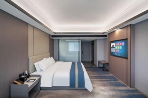A modern hotel room with a large bed, a bedside table, a flat-screen TV, and a view of the hallway.