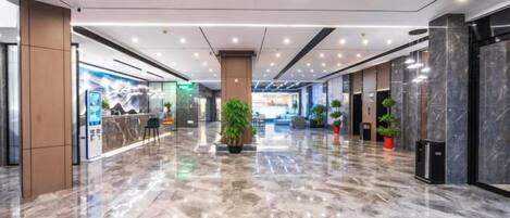 A spacious lobby with a marble floor, a reception desk, and potted plants.