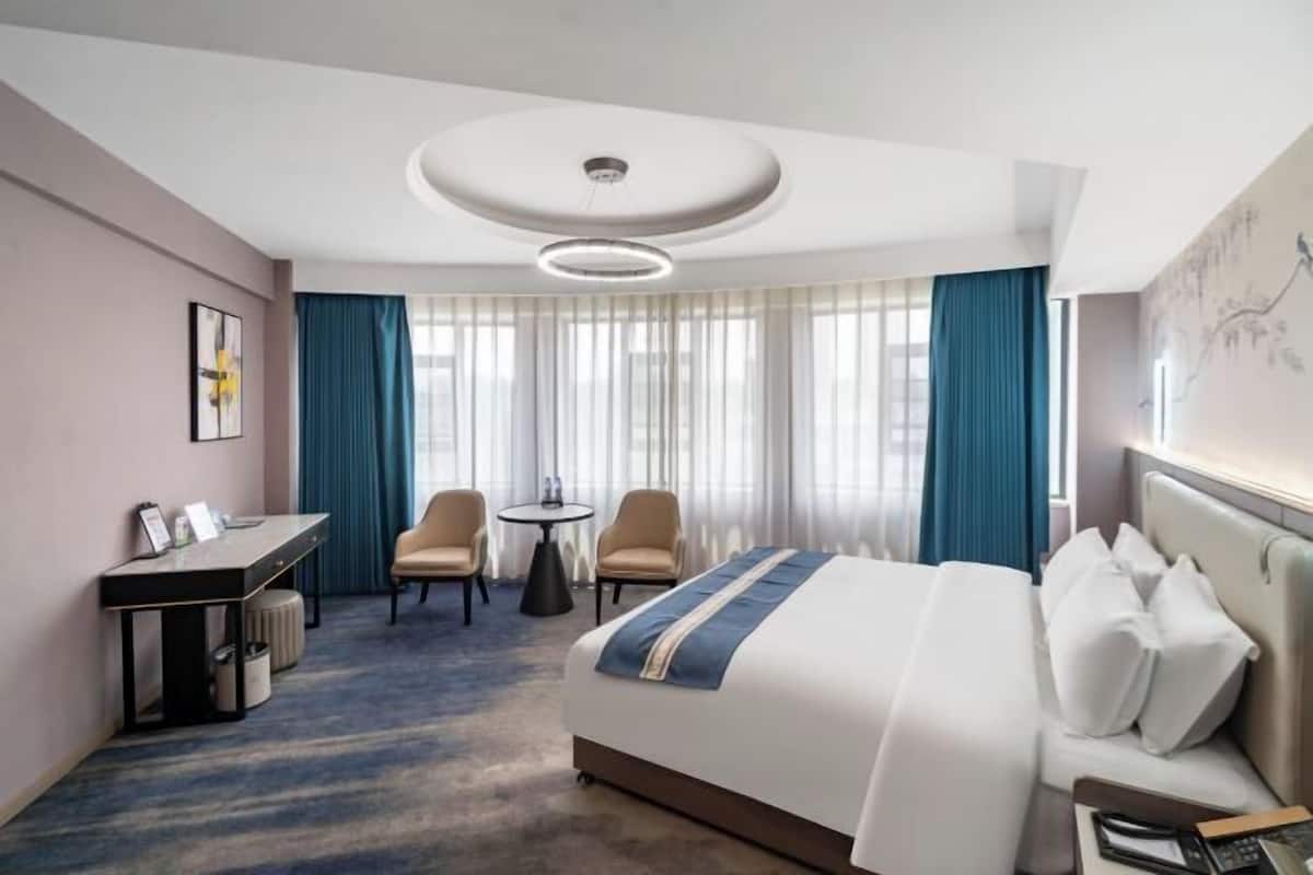 Quarto de hotel com uma cama grande, uma escrivaninha, duas cadeiras e uma mesa pequena.