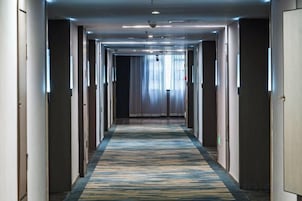 A hotel hallway with a carpeted floor, doors on both sides, and a light fixture on the ceiling.