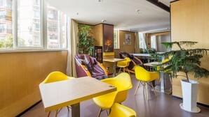 Moderni hotellin aula, jossa on keltaisia tuoleja ja pöytiä, suuret ikkunat ja sisätiloissa olevia kasveja.