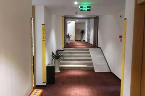 Un couloir avec un sol recouvert de moquette, un escalier et une porte au fond.