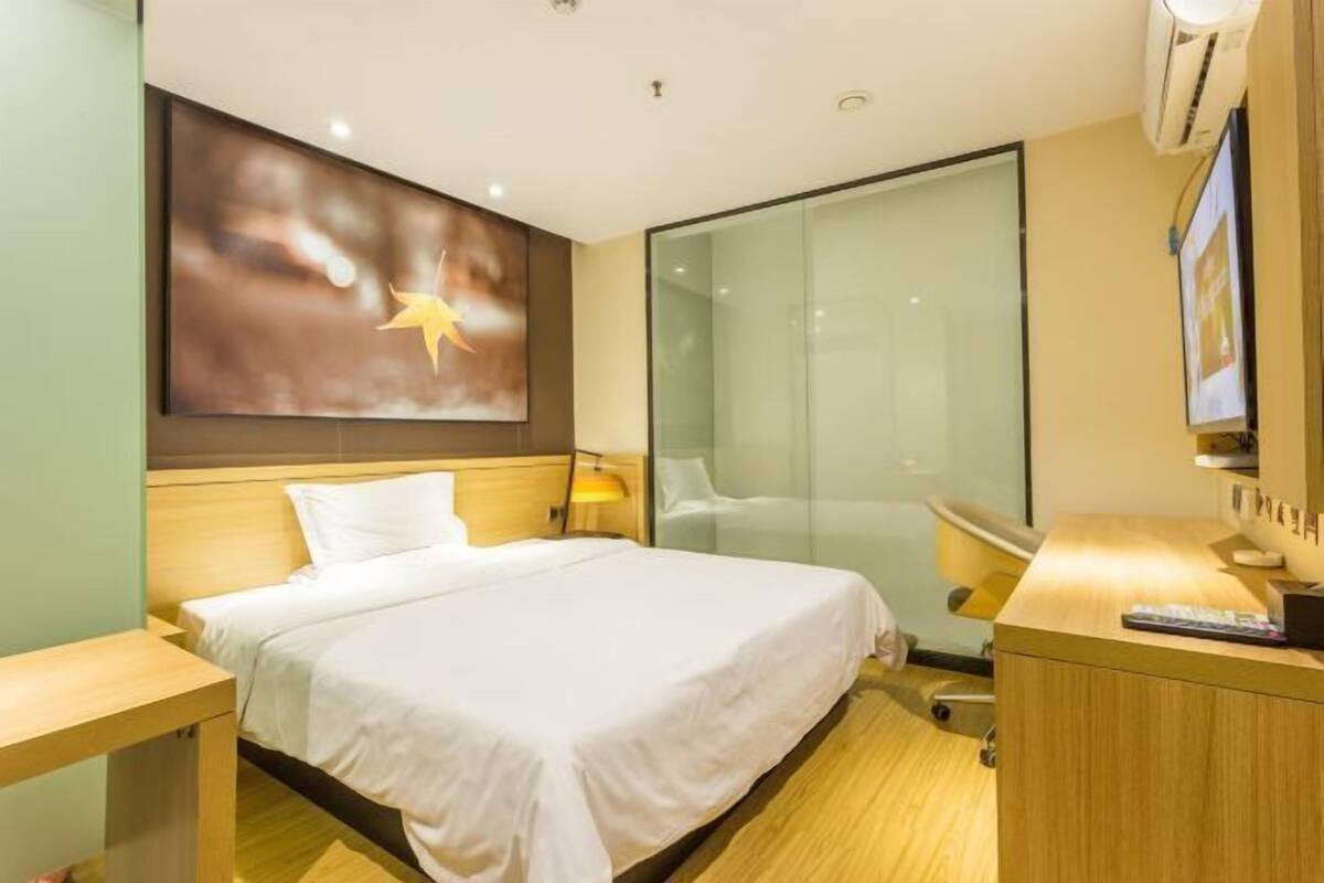 Hotellihuone, jossa on sänky, työpöytä, tuoli, televisio ja seinälle kiinnitetty taideteos.