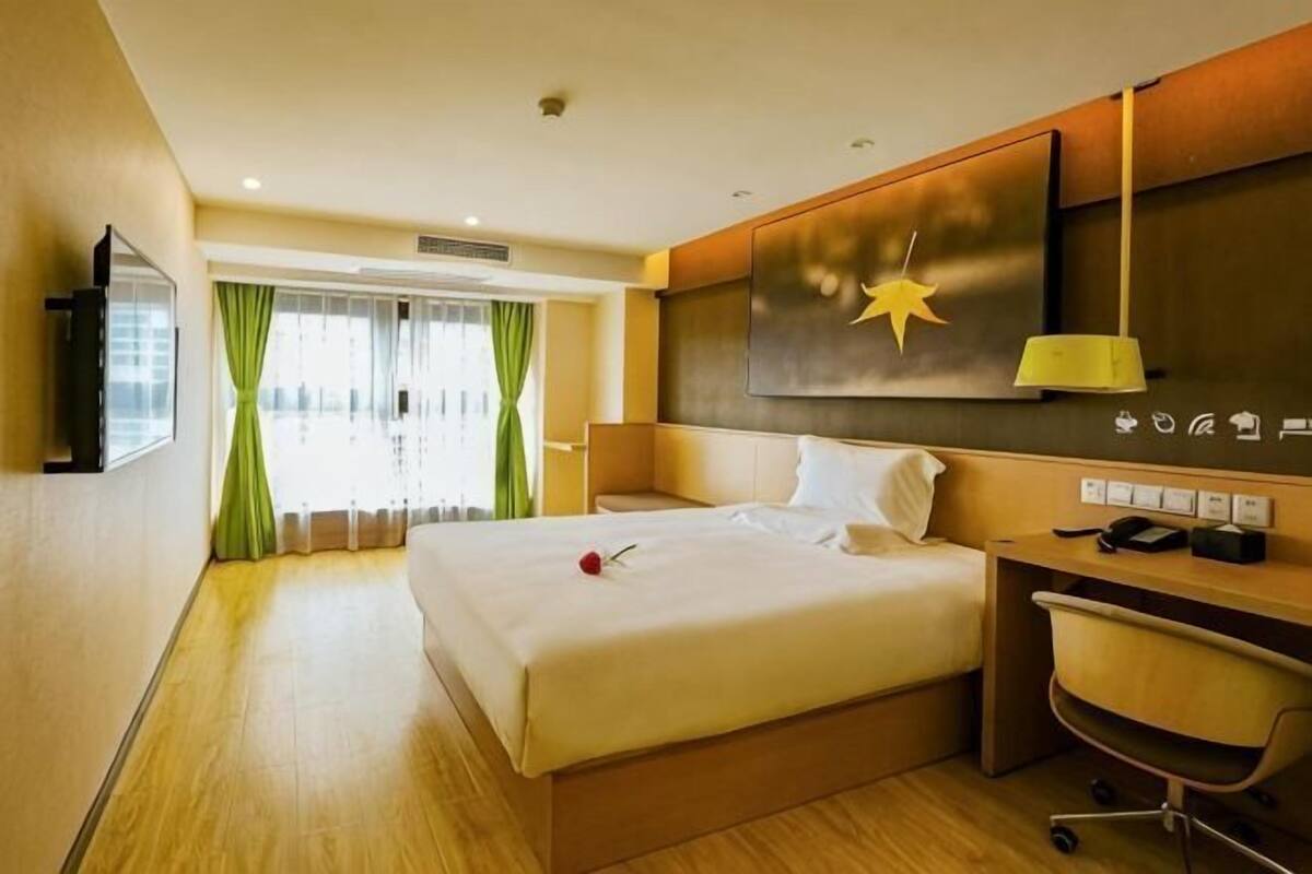 Hotellihuone, jossa on sänky, työpöytä, tuoli ja suuri ikkuna, jossa on verhot.