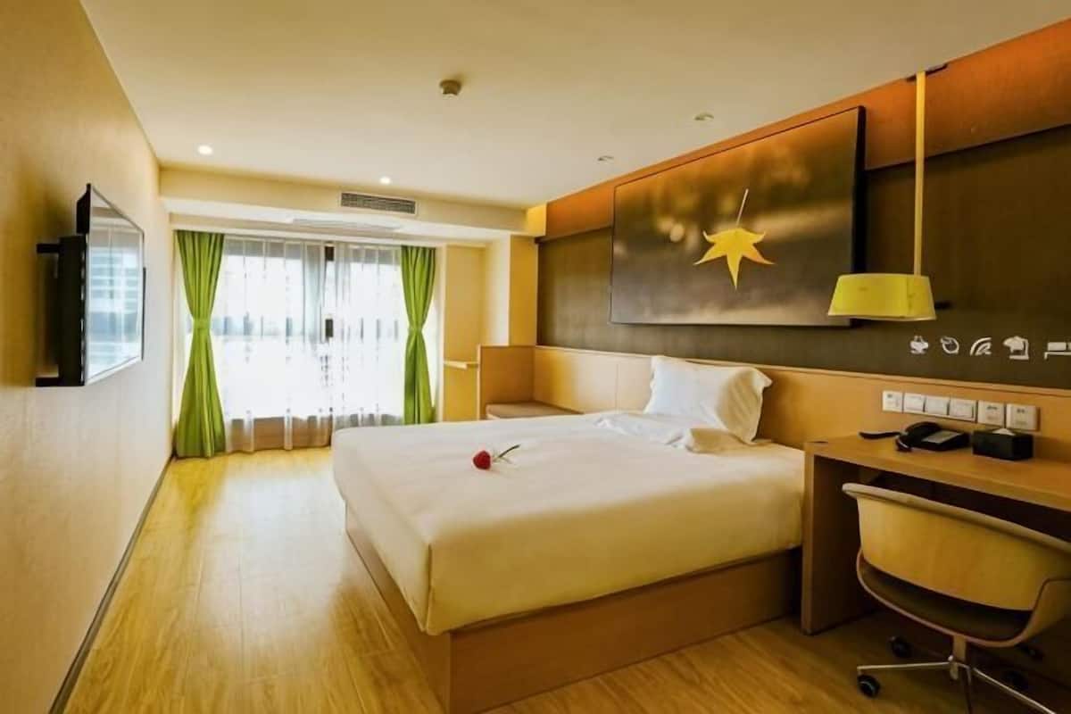 A hotel room with a bed, desk, chair, and a large window with curtains.
