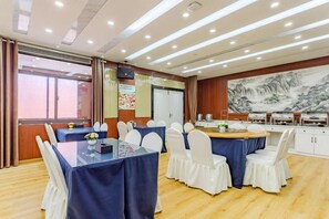 A conference room with tables and chairs, a large painting on the wall, and a buffet area.