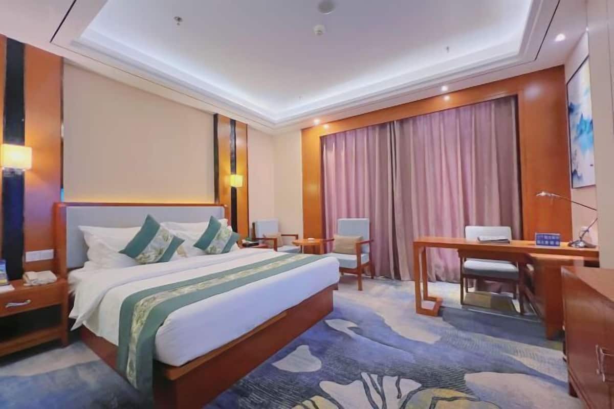 A hotel room with a large bed, a desk, a chair, a lamp, and a painting on the wall.