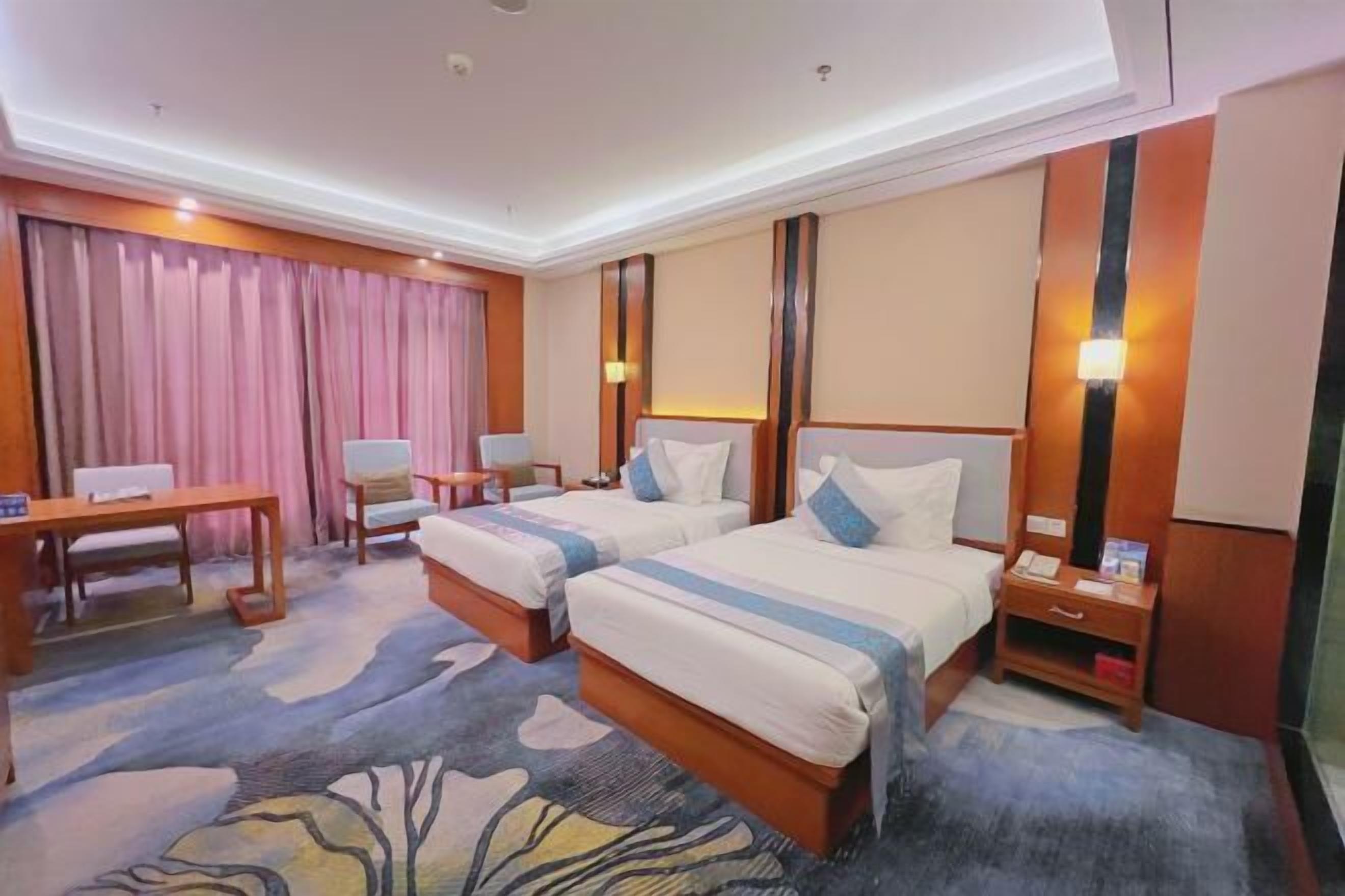 Ein Hotelzimmer mit zwei Betten, einem Schreibtisch, einem Stuhl, einem Nachttisch und einem großen Fenster mit Vorhängen.