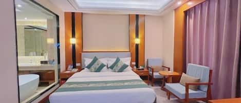 A hotel room with a large bed, bedside tables, a chair, a desk, a mirror, and a bathroom with a sink and toilet.