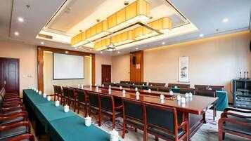 A conference room with a long table, chairs, a projector screen, and a television.