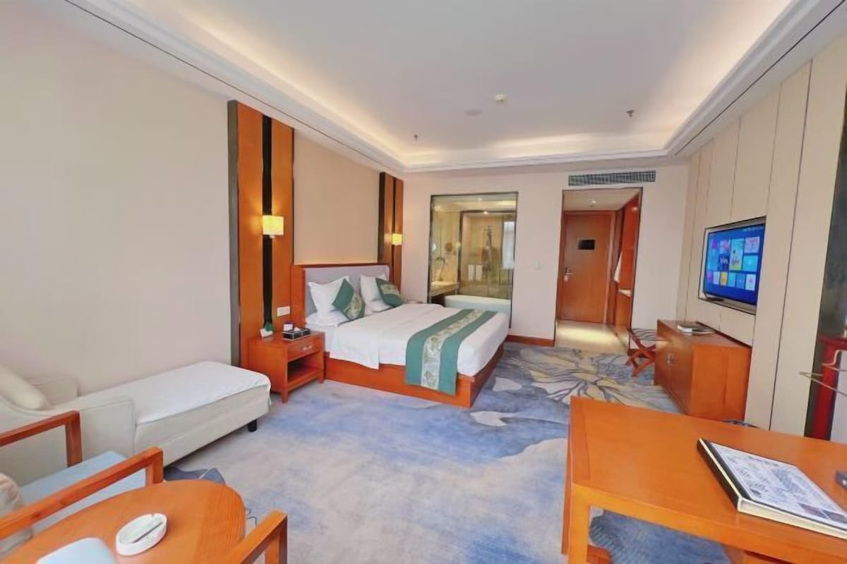 A hotel room with a bed, a sofa, a desk, and a television.
