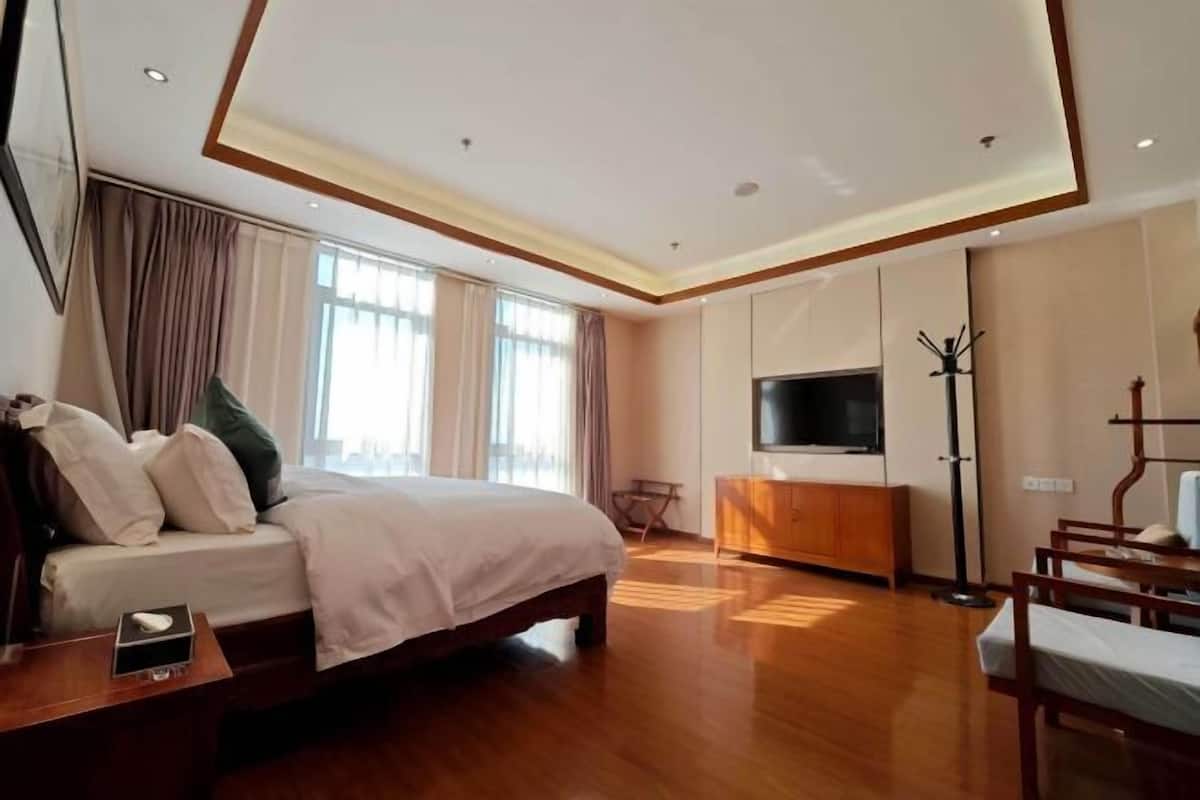 A modern hotel room with a large bed, wooden flooring, a flat-screen TV, a wardrobe, and a seating area with chairs.