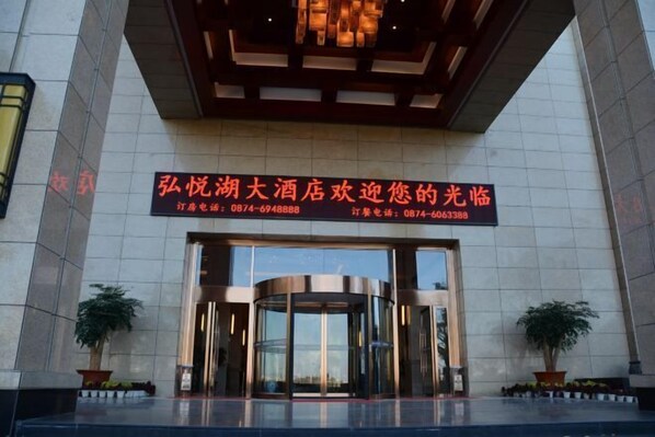 A hotel entrance with a revolving door, potted plants, and a sign with contact information. - Hongyuehu Hotel (Luliang)