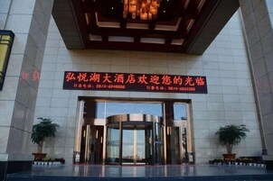 A hotel entrance with a revolving door, potted plants, and a sign with contact information.