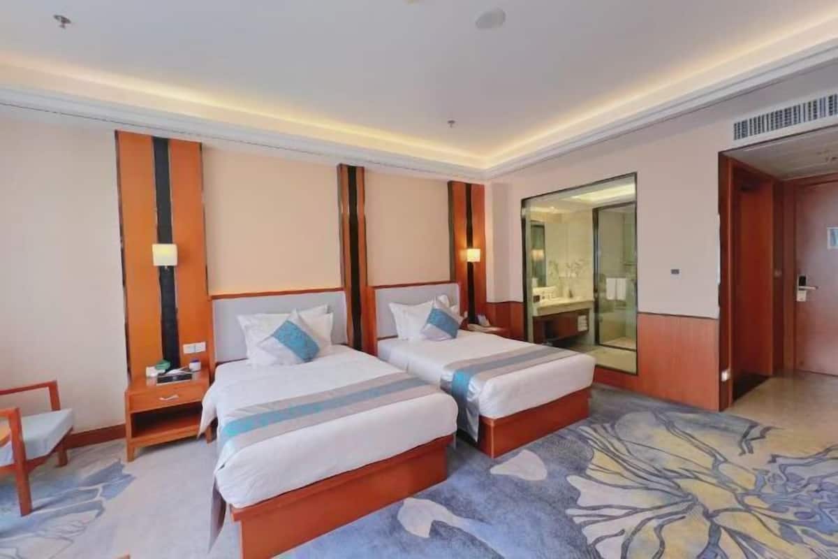 A hotel room with two beds, a nightstand, a chair, and a large mirror.
