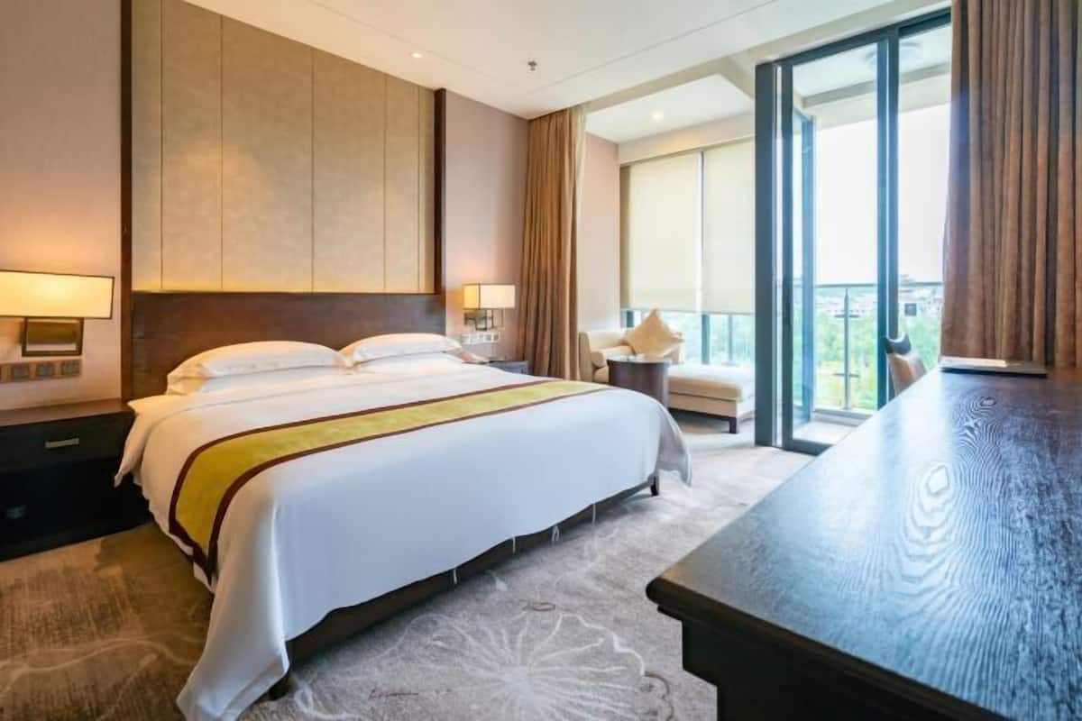 Ein Hotelzimmer mit einem großen Bett, einem Schreibtisch, einem Sessel und einem Balkon mit Blick.