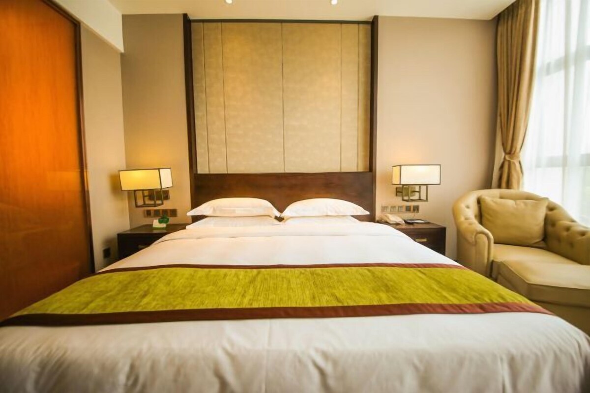 A hotel room with a large bed, two bedside tables with lamps, a sofa, and a large window with curtains.