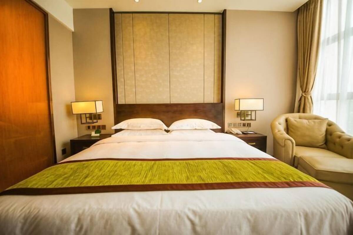 Ein Hotelzimmer mit einem großen Bett, zwei Nachttischen mit Lampen, einem Sofa und einem großen Fenster mit Vorhängen.