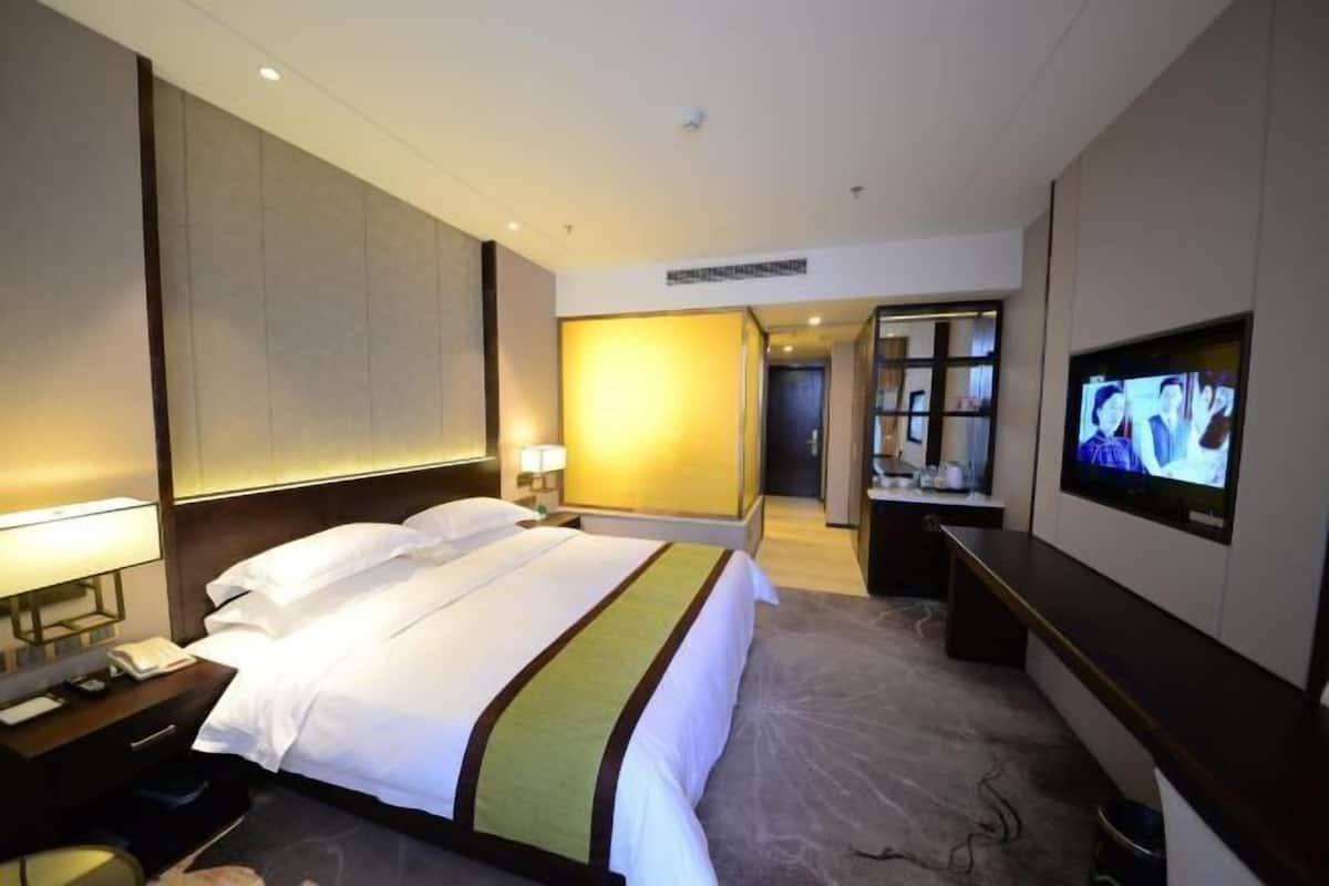Ein Hotelzimmer mit Bett, Nachttisch, Fernseher und Blick auf den Flur.