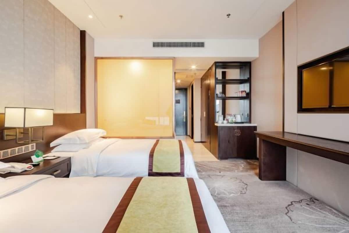 Ein Hotelzimmer mit zwei Betten, einem Schreibtisch mit Lampe, einer Minibar und einem Fernseher.