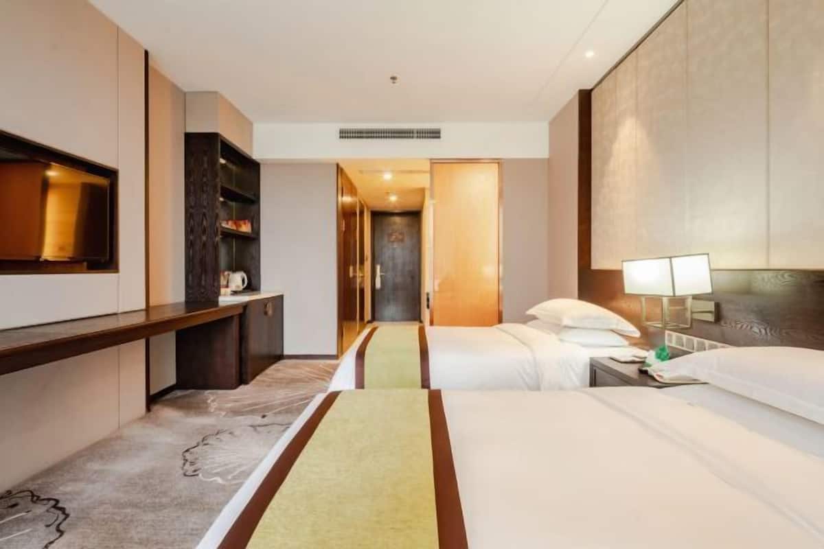Ein Hotelzimmer mit Bett, Nachttisch, Lampe und einem an der Wand befestigten Fernseher.