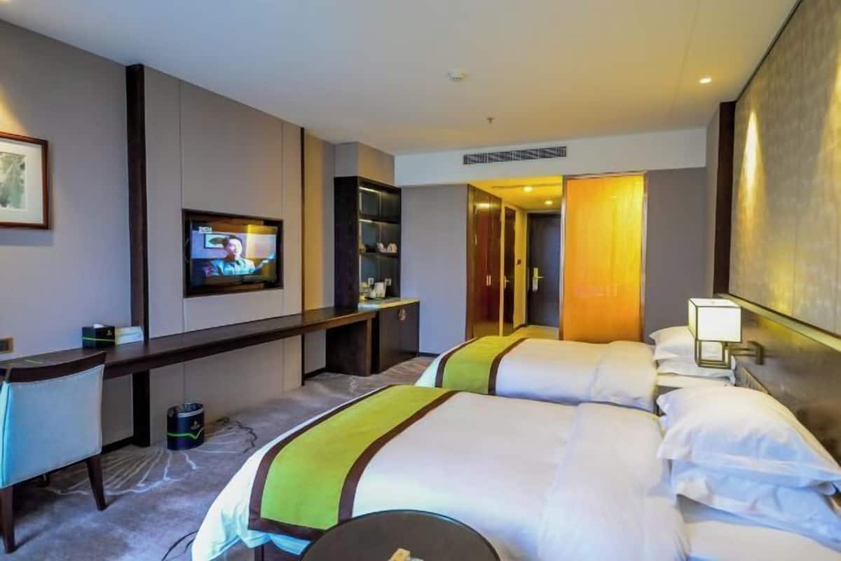 Ein Hotelzimmer mit zwei Betten, einem Schreibtisch, einem Fernseher und einem Spiegel.