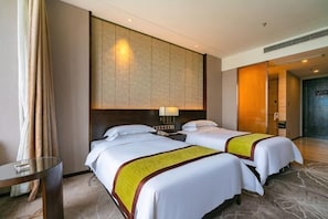 Een hotelkamer met twee bedden, een nachtkastje, een lamp, een glazen tafel en uitzicht op de gang.