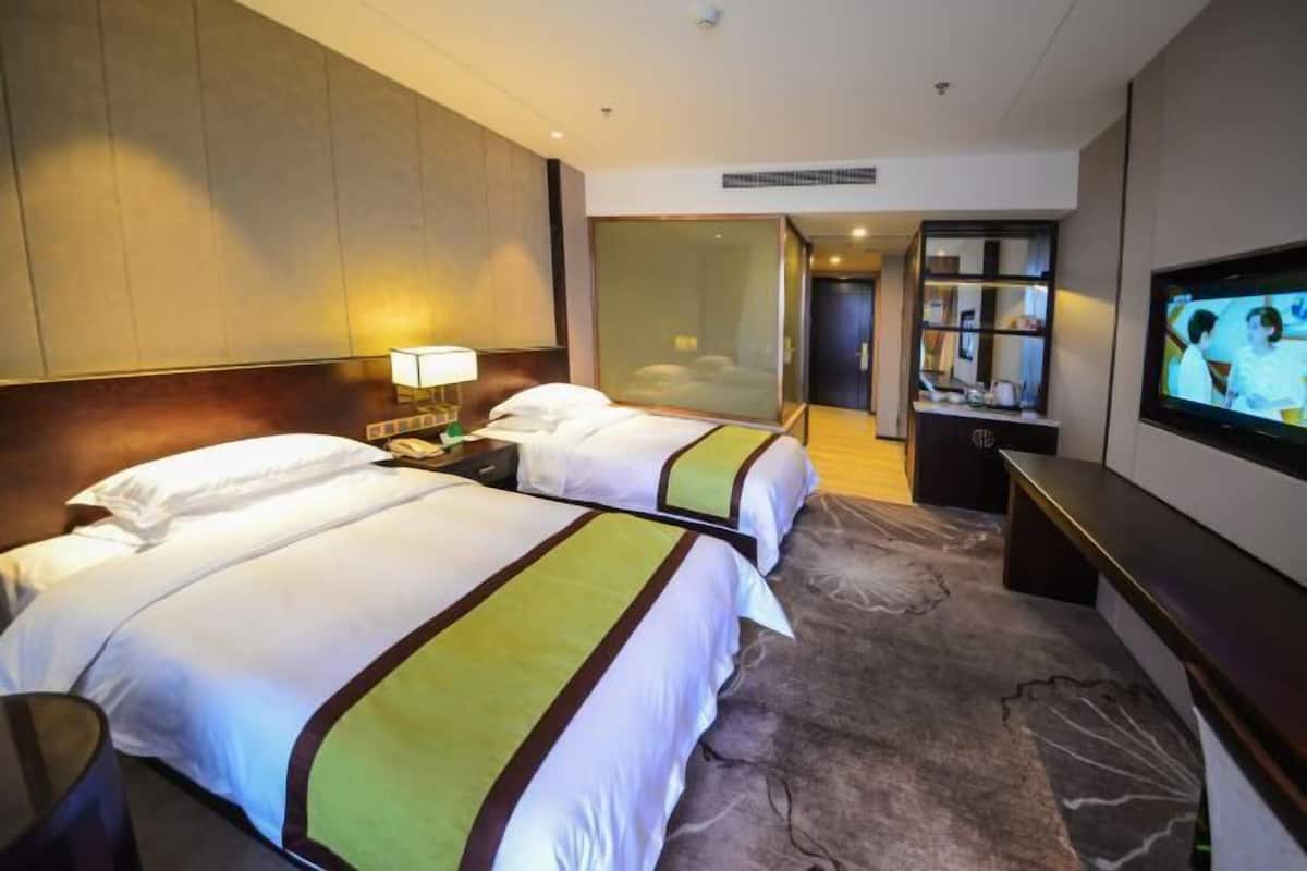 Ein Hotelzimmer mit zwei Betten, einem Fernseher, einer Minibar und einem Spiegel.