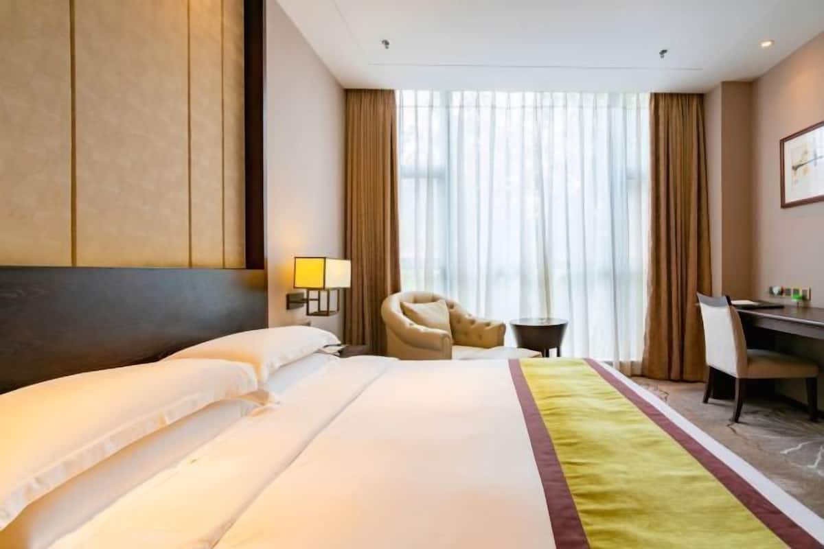 Ein Hotelzimmer mit einem großen Bett, einem Schreibtisch, einem Stuhl und einem Fenster mit Vorhängen.