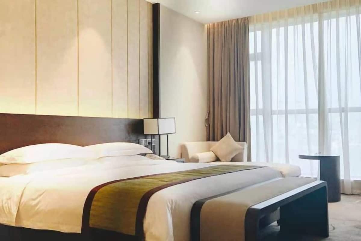 Ein Hotelzimmer mit einem großen Bett, einem Nachttisch, einem Sessel und einem Fenster mit Vorhängen.