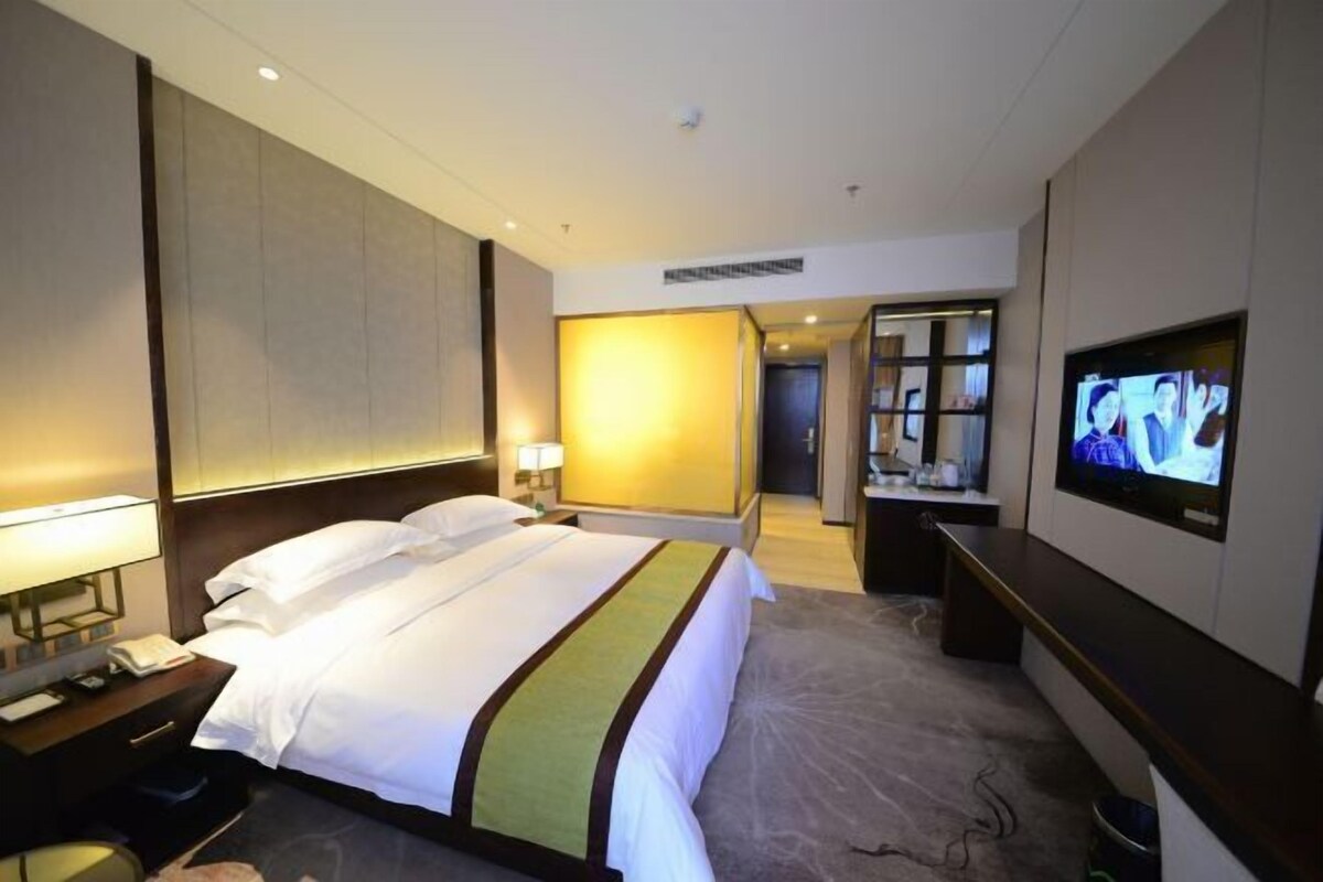 A hotel room with a bed, a television, a desk with a lamp, and a bathroom visible through an open door.