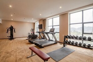 Een sportschool met loopbanden, een bank, een squat rek en een televisie aan de muur.
