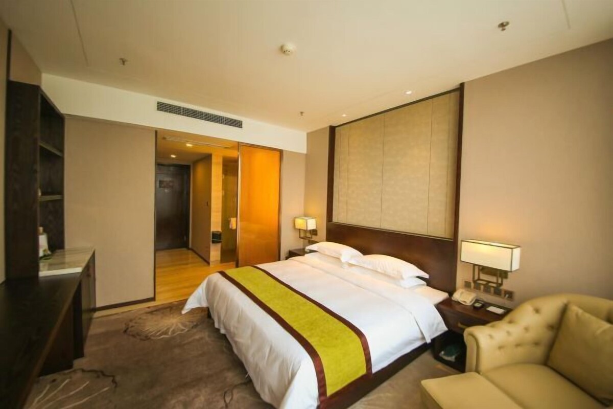 A hotel room with a bed, bedside tables, a chair, and a view of the hallway.