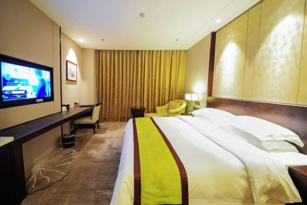 A hotel room with a bed, a desk with a television, a chair, and a lamp.