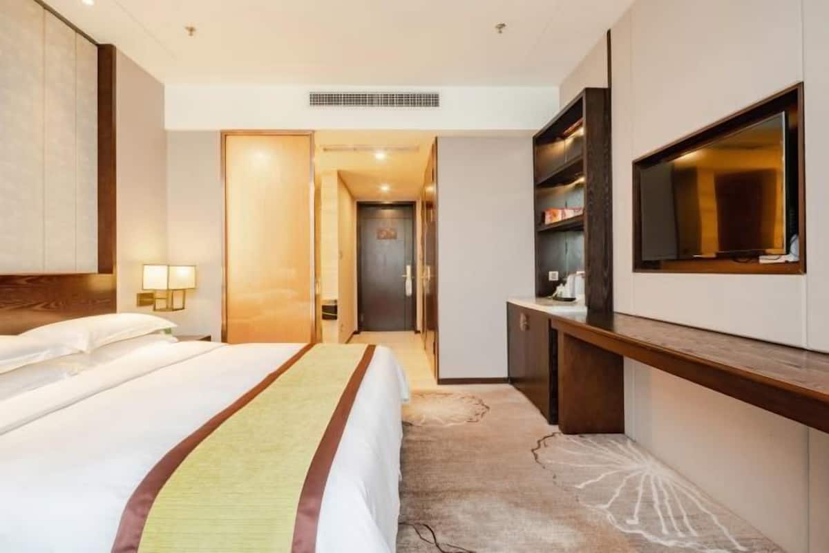 Ein Hotelzimmer mit Bett, Fernseher, Schreibtisch und Kleiderschrank.