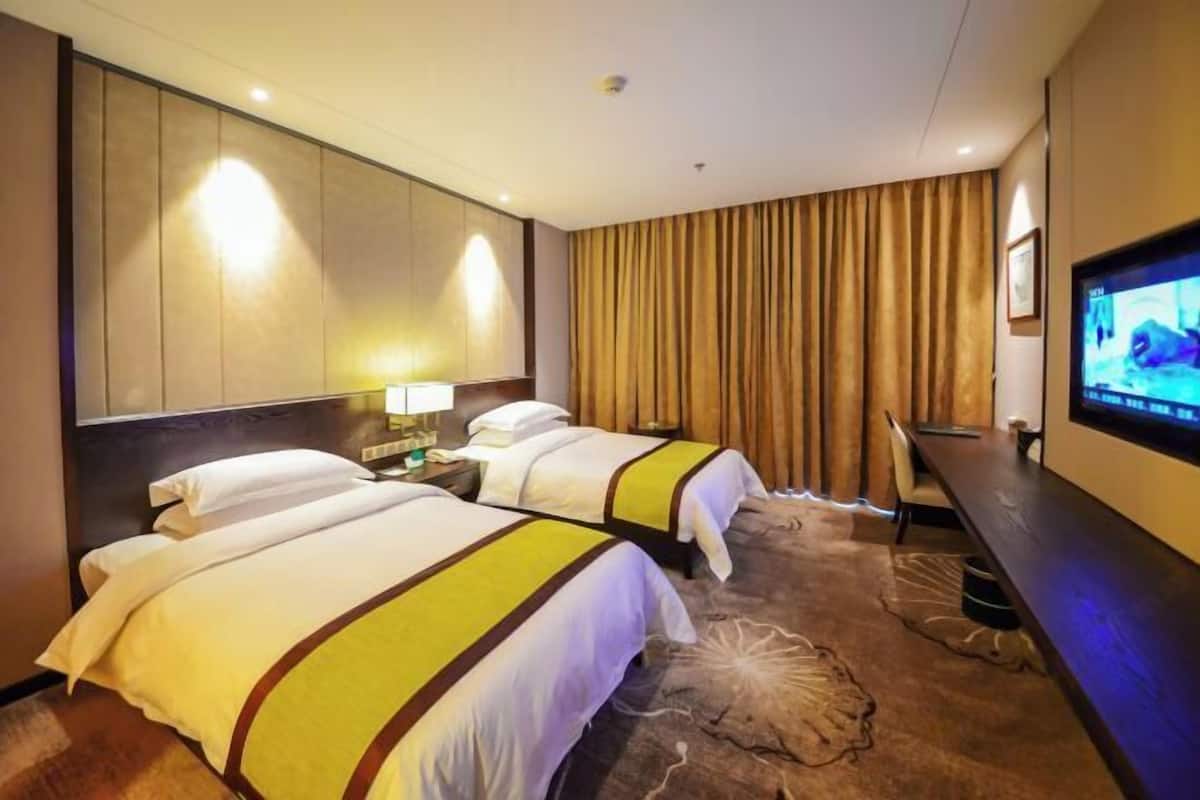 Ein Hotelzimmer mit zwei Betten, einem Fernseher, einem Schreibtisch und einem großen Fenster mit Vorhängen.
