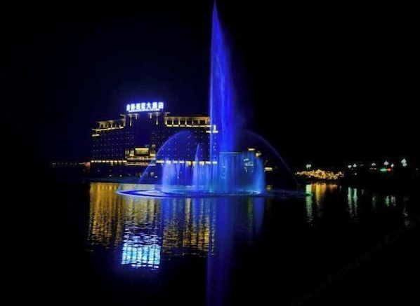 A nighttime view of a building with illuminated signage and a fountain in the foreground.