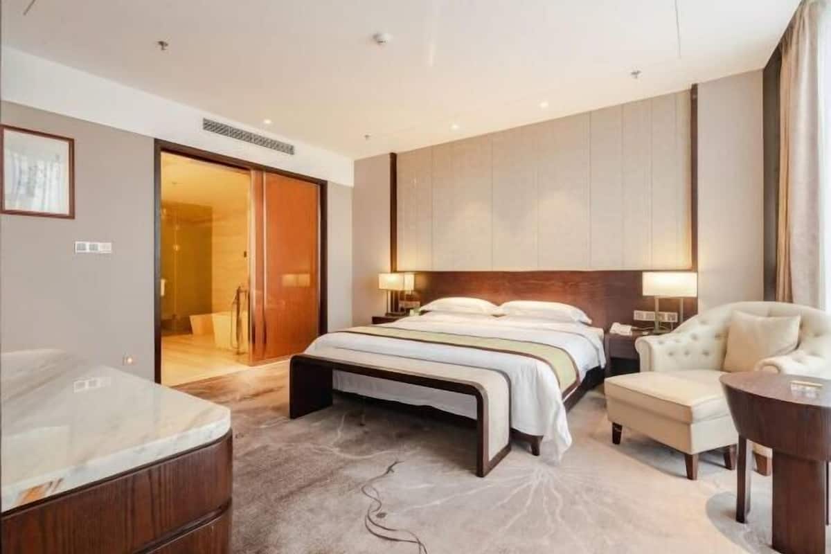Ein Hotelzimmer mit einem großen Bett, einer Sitzecke mit einem Sessel, einem Schreibtisch und einem Badezimmer mit einer Marmortonne.