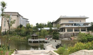 A traditional Chinese-style building with a garden, a pond, and a bridge.