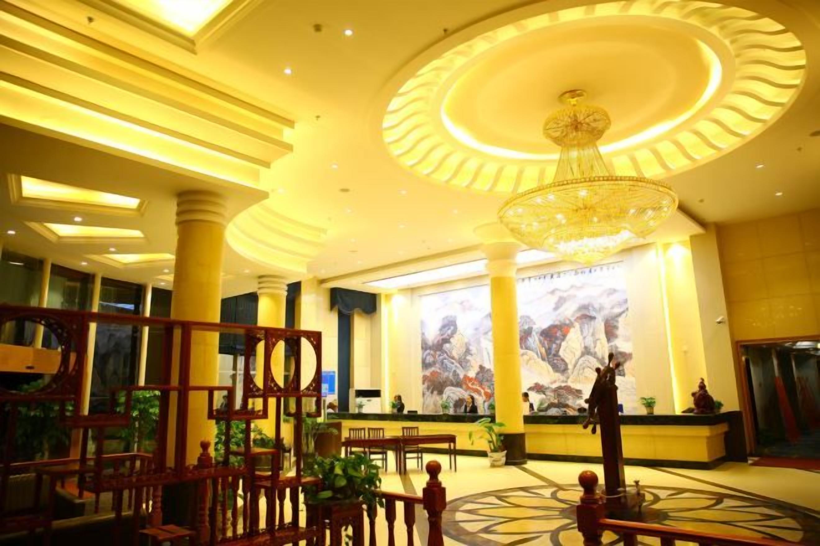 A hotel lobby with a large chandelier, a reception desk, and a large mural on the wall.